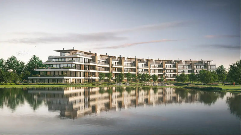 Complejo moderno de apartamentos de varios pisos con exterior beige y blanco, balcones de vidrio y agua reflectante en el frente.